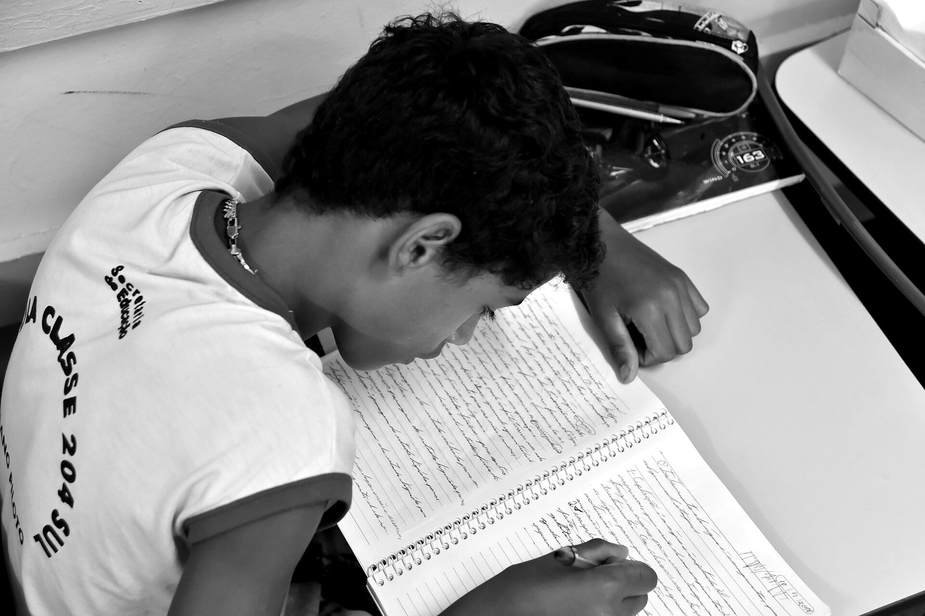 Estudante debruçado sobre o caderno, em preto e branco