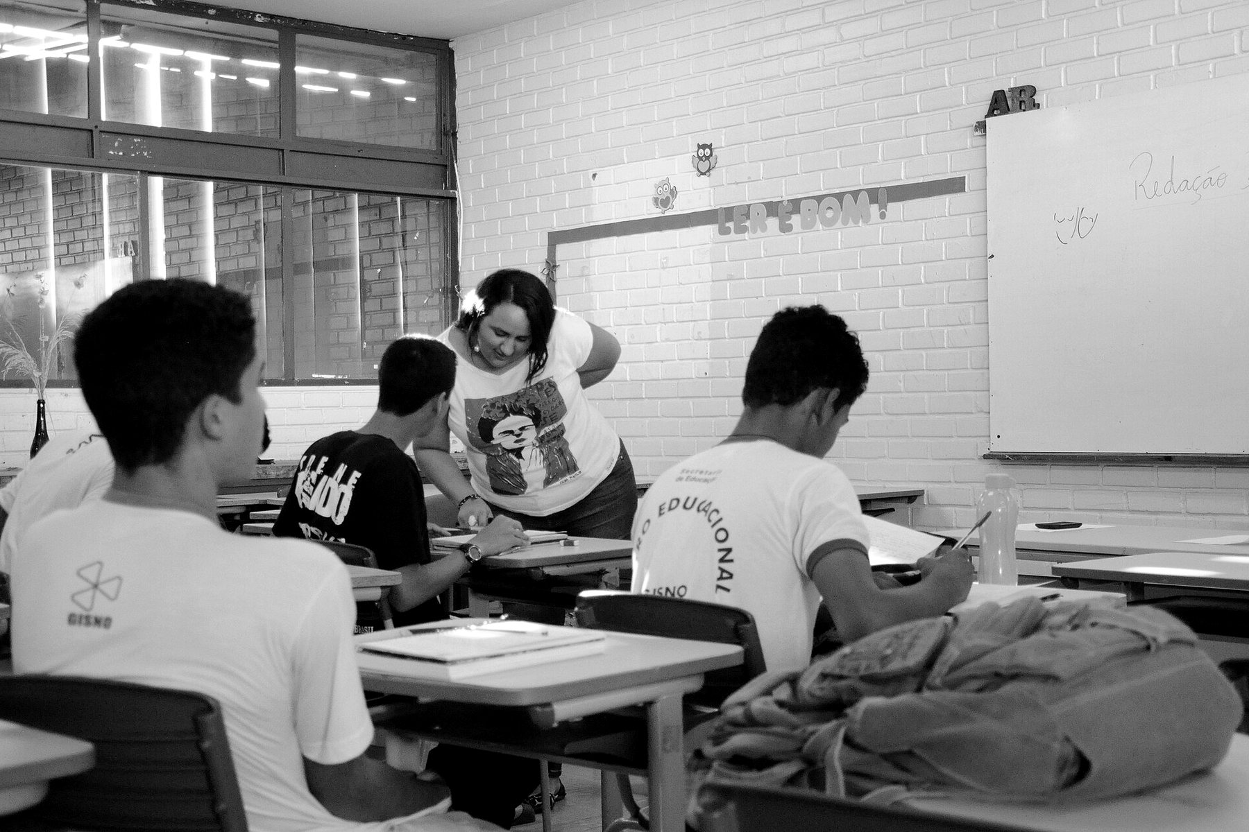 Professora atendendo estudantes do ensino médio nas carteiras, em preto e branco