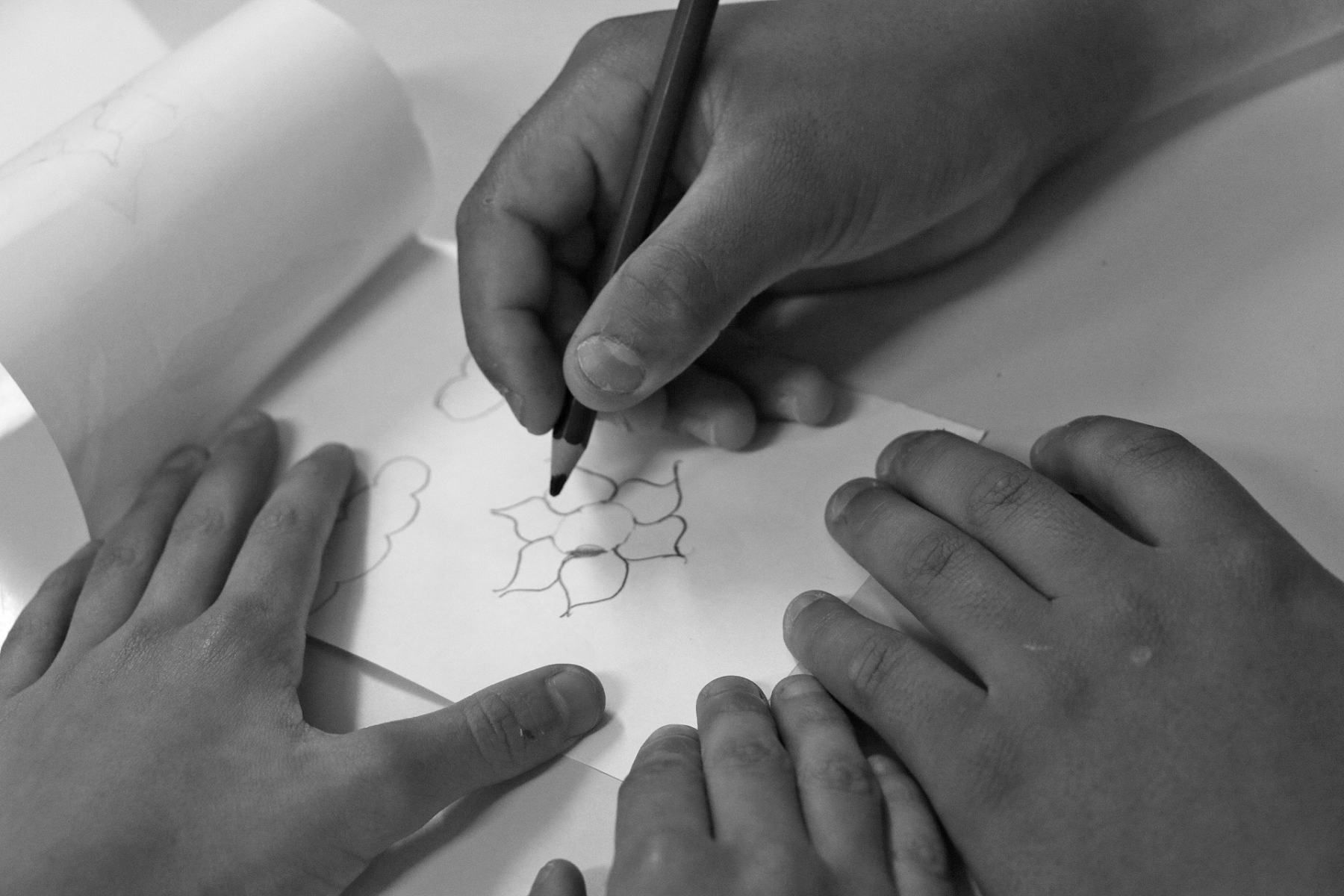 Mãos de um estudante desenhando a lápis sobre o papel, em preto e branco